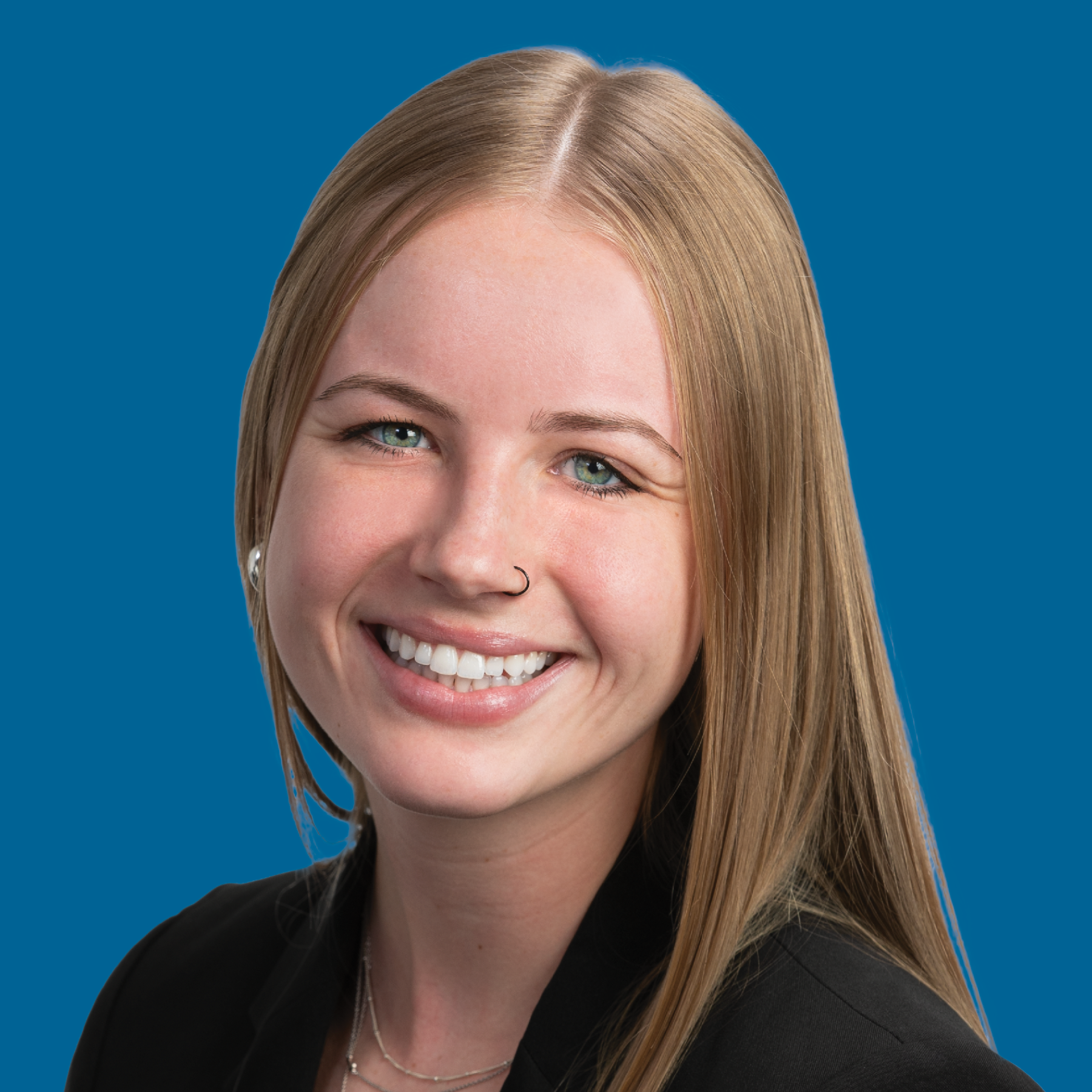 A smiling professional with light brown hair wearing a black-and-white grid pattern blazer against a blue background.