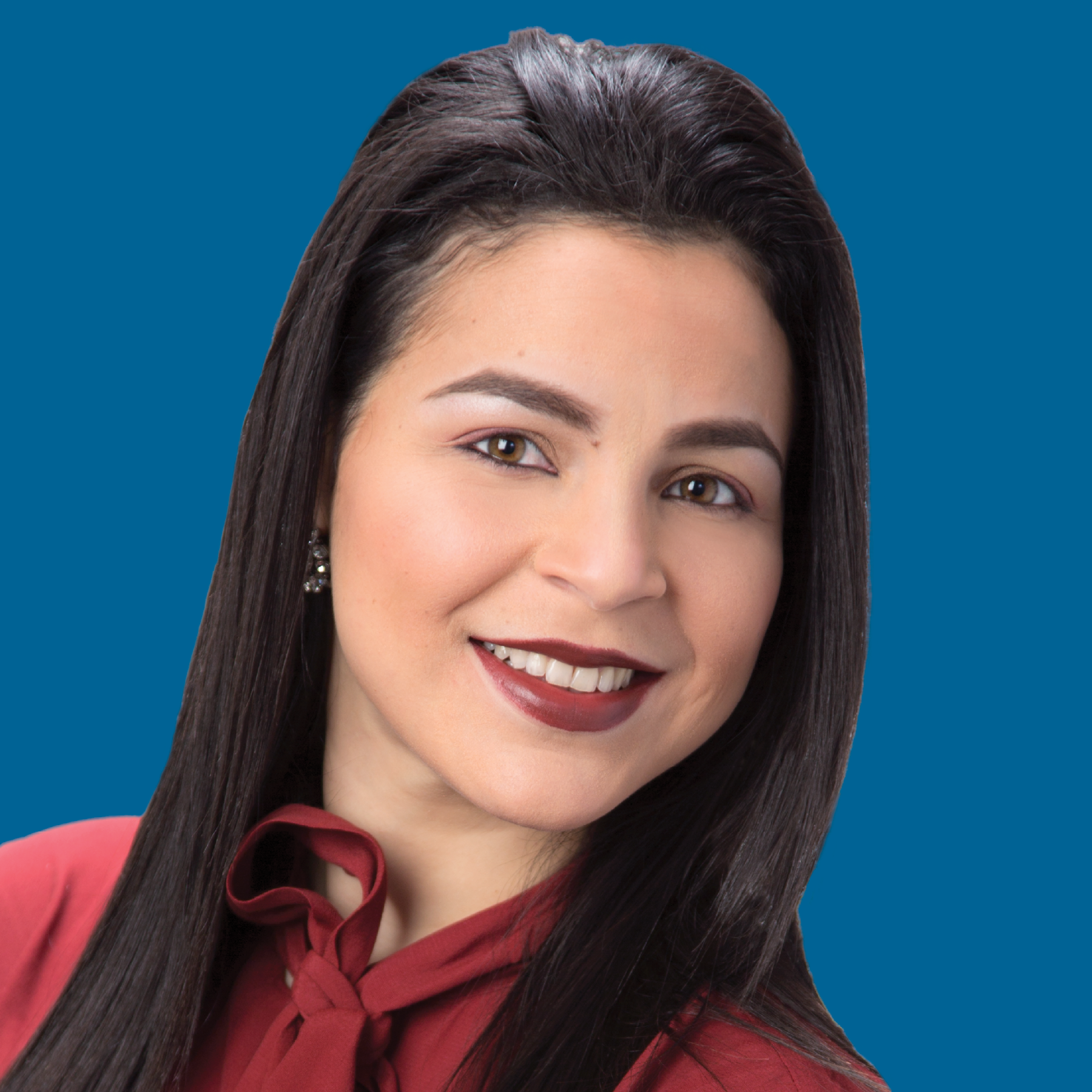 A smiling person with long dark hair wearing a maroon top against a solid blue background.