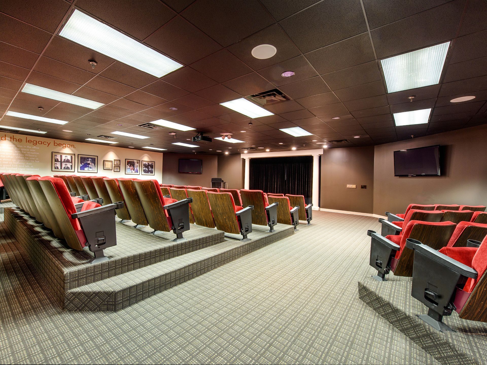 A movie theater featuring red-cushioned seats arranged in tiered rows on a patterned carpeted floor.