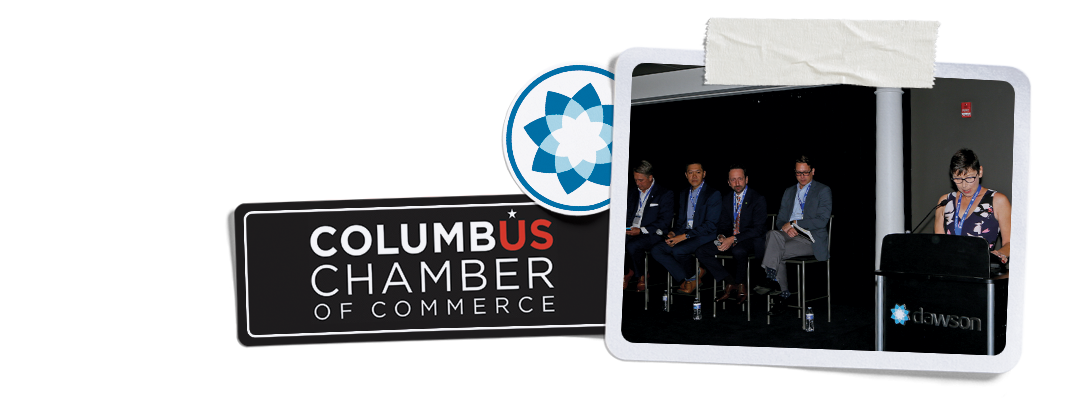 The Columbus Chamber of Commerce logo next to a framed photograph of four people sitting on a stage at an event.