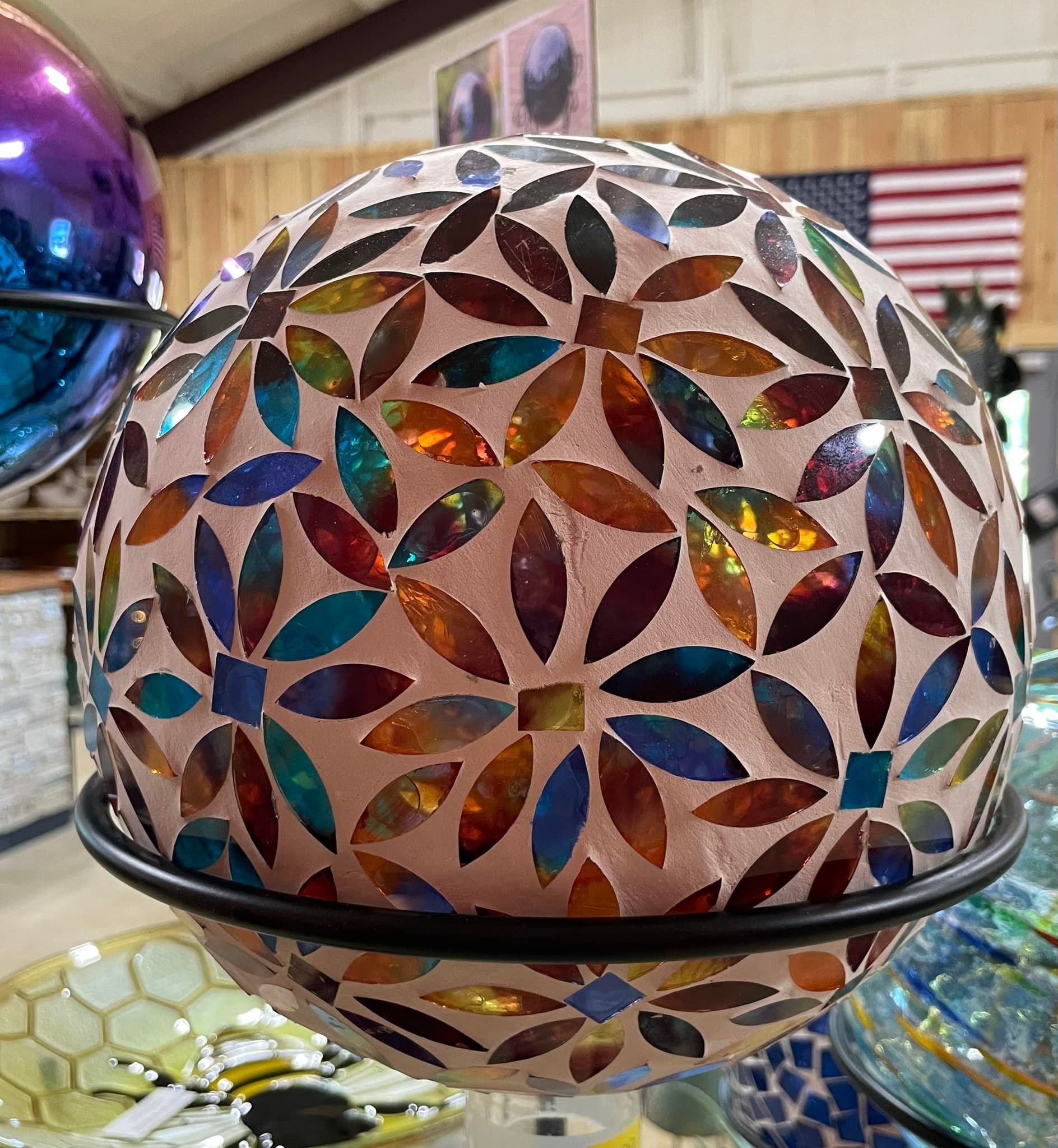 Mosaic glass gazing ball in a metal stand, displaying a floral pattern with iridescent petals.
