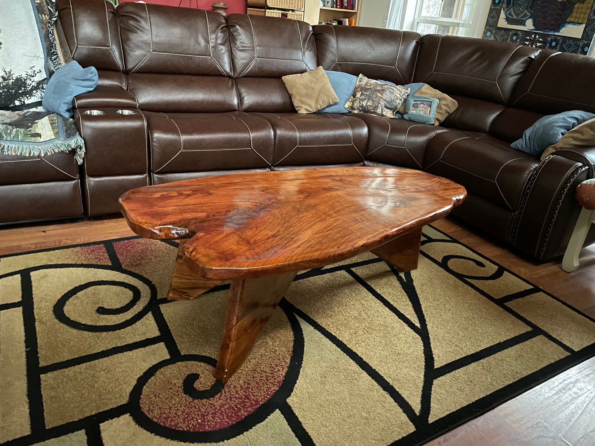 Wooden coffee table in front of a brown leather sectional sofa on a patterned rug.