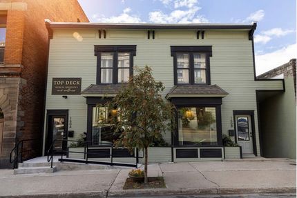 Storefront with pale green facade, large windows, and a sidewalk tree in front of it.
