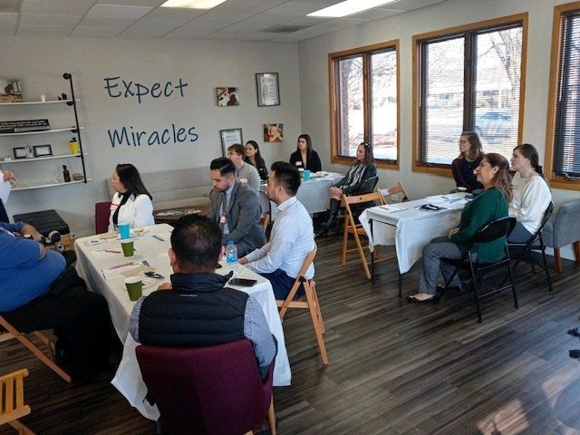 People seated at tables in a bright meeting room with “Expect Miracles” on the wall.