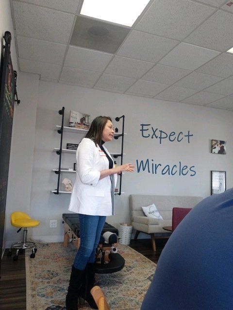 Woman in white coat speaking in an office with “Expect Miracles” on the wall