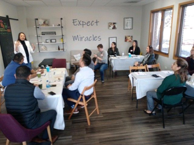 Small group meeting in a bright room, with people seated around tables and “Expect Miracles” on the wall