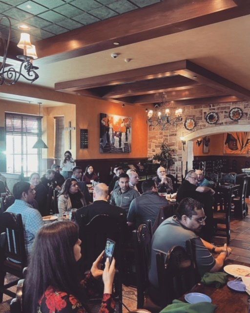 Crowded bar or cafe interior with many people seated at tables, warm lighting, and wall decor