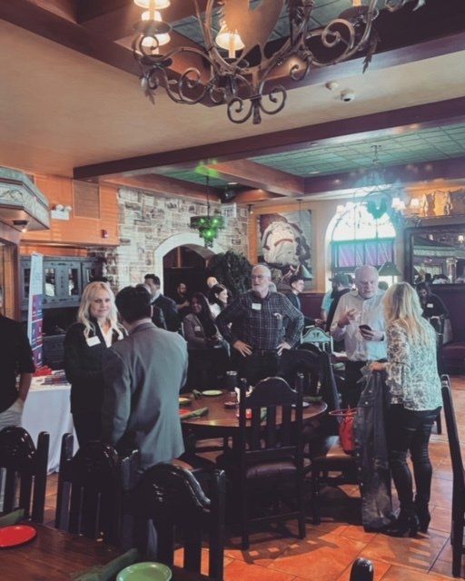 People seated and standing in a cozy restaurant with stone walls and hanging chandeliers.