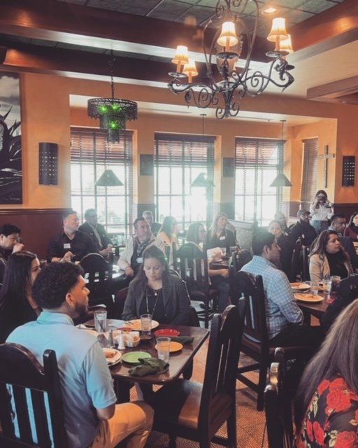 People dining in a warmly lit restaurant with dark wood tables and chairs under a chandelier.