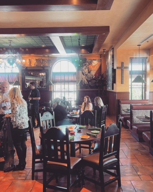 Cozy restaurant interior with wooden tables, tiled floor, arched window, and diners seated near a bar.