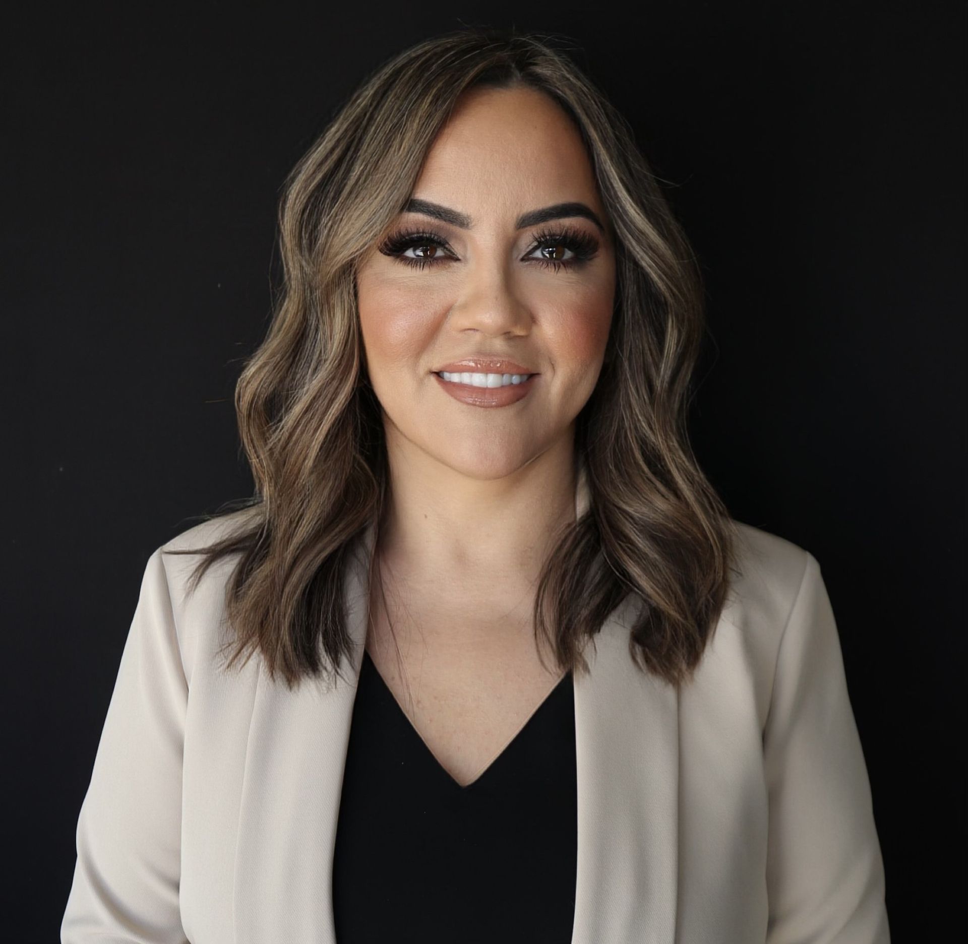 Smiling woman in a beige blazer and black top against a dark background