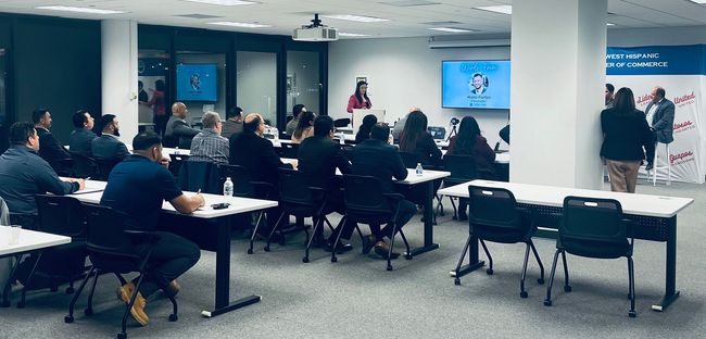 Conference room meeting with seated attendees and a presenter beside a large screen