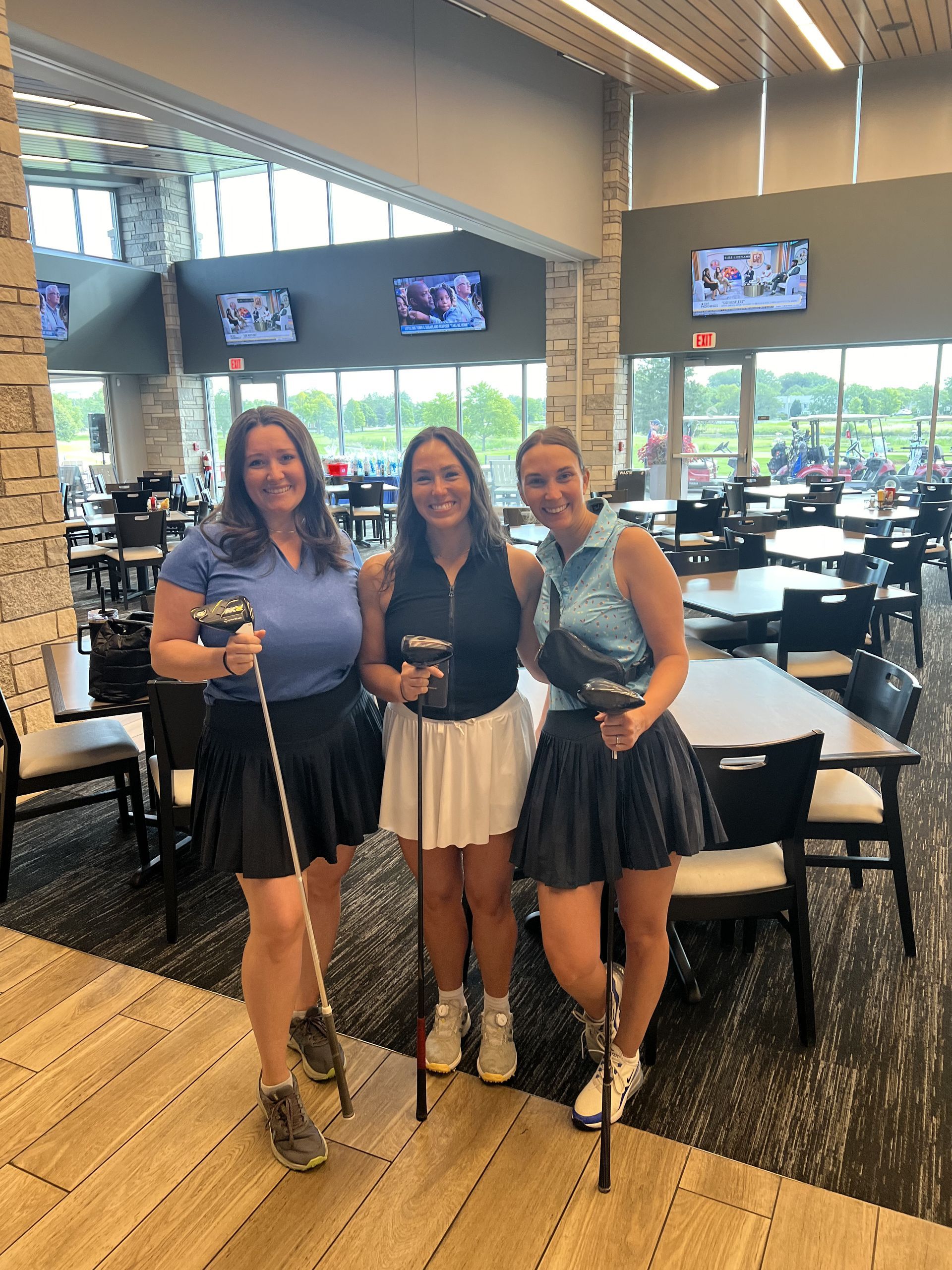 Three friends posing with golf clubs in a bright café or clubhouse dining area