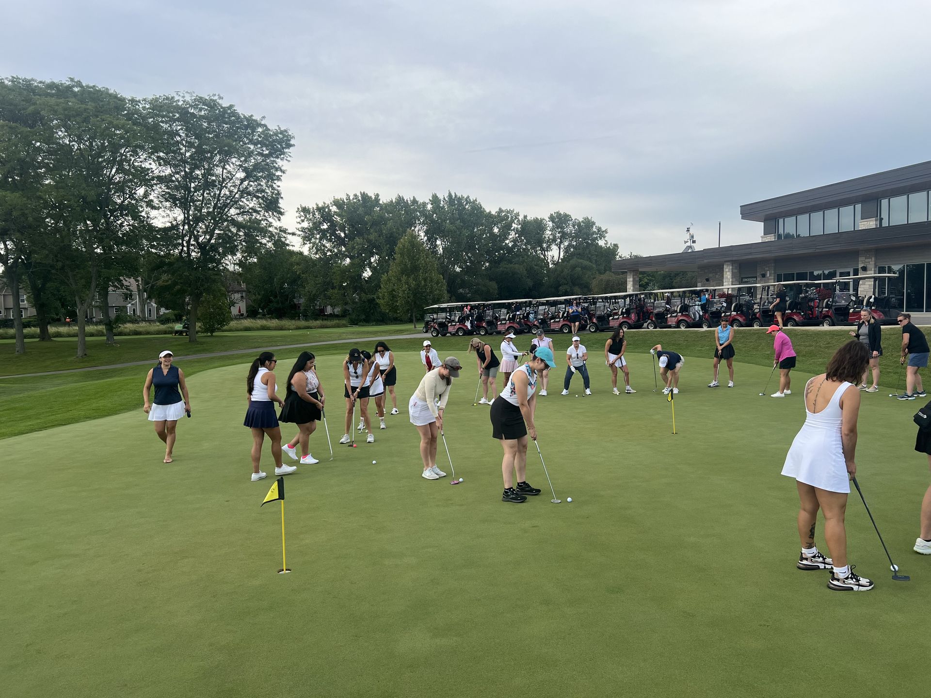 People practicing drills on a grassy field beside a building under a cloudy sky.
