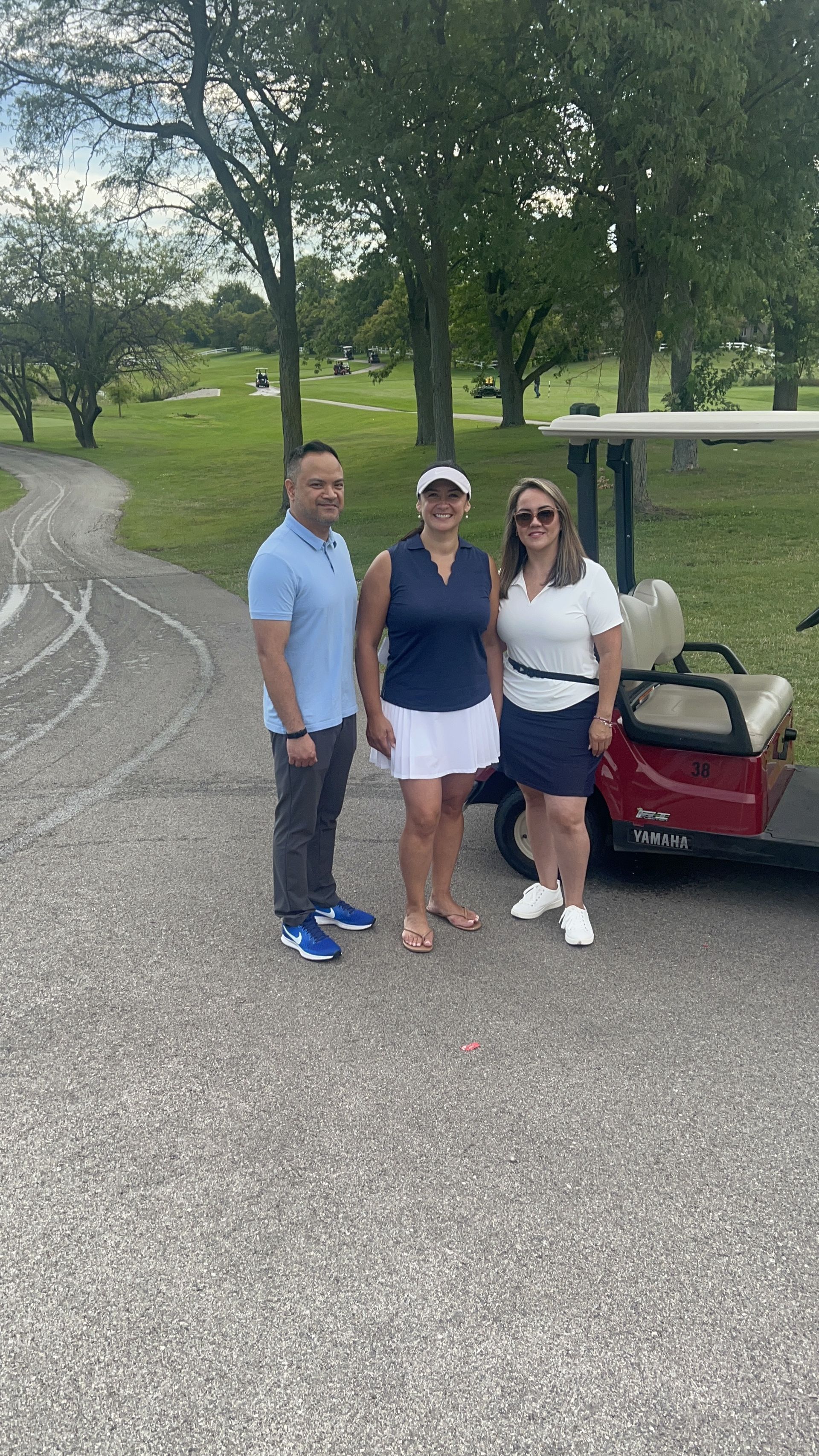 Three people standing beside a golf cart on a paved path in a park.