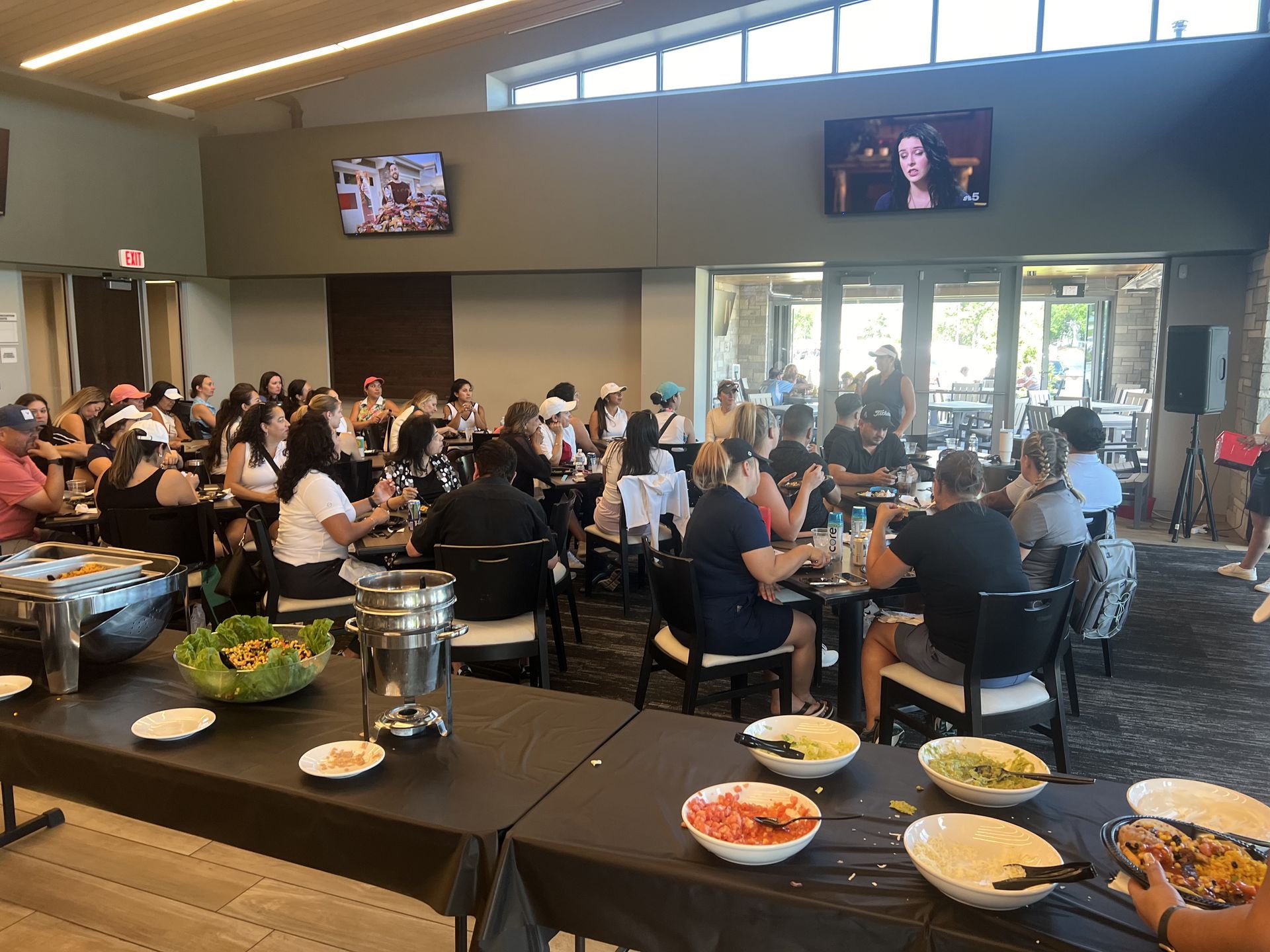 Crowded dining hall with people eating at tables and buffet dishes in the foreground