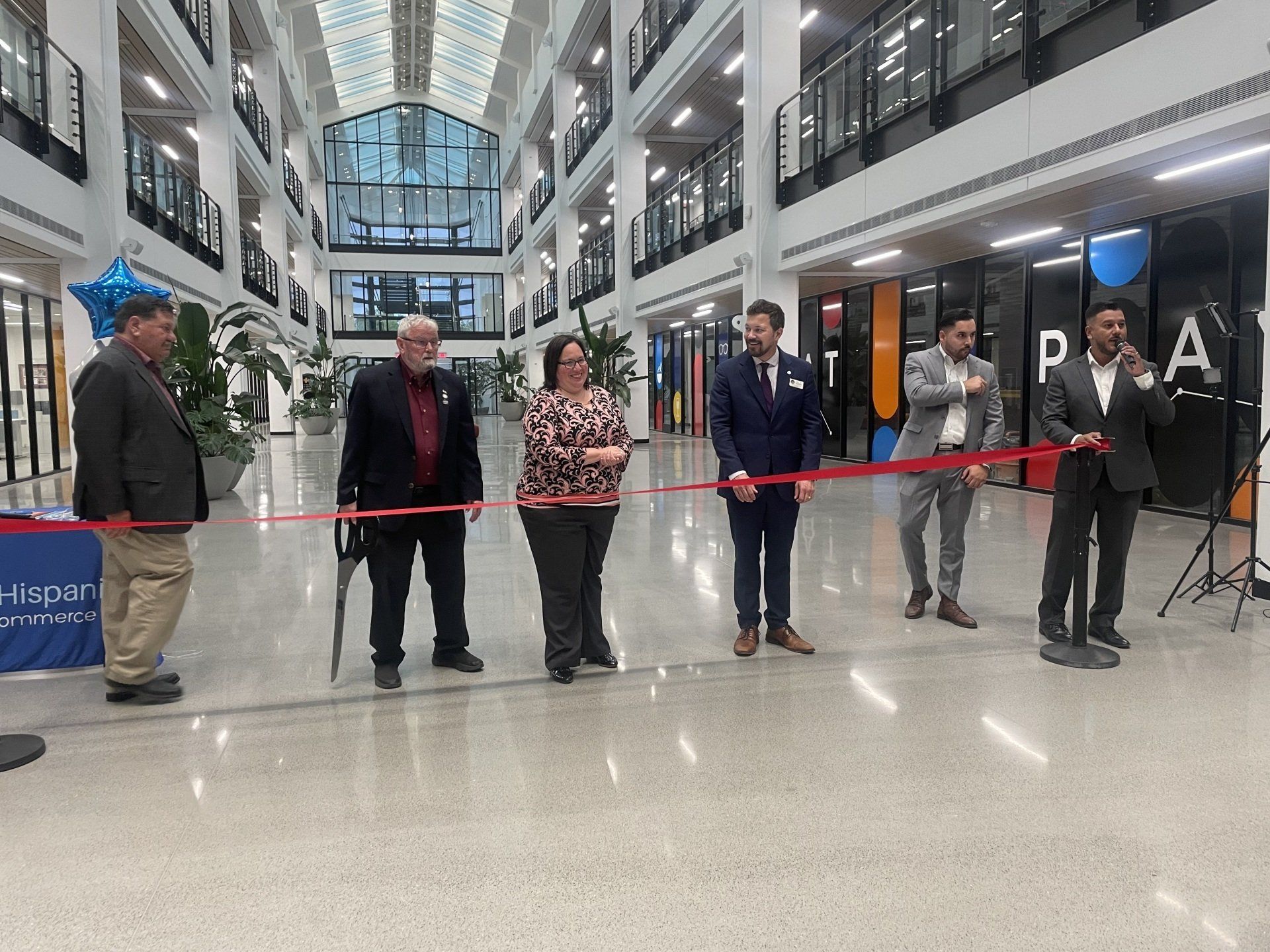 People standing behind a red ribbon in a bright atrium during a ribbon-cutting ceremony