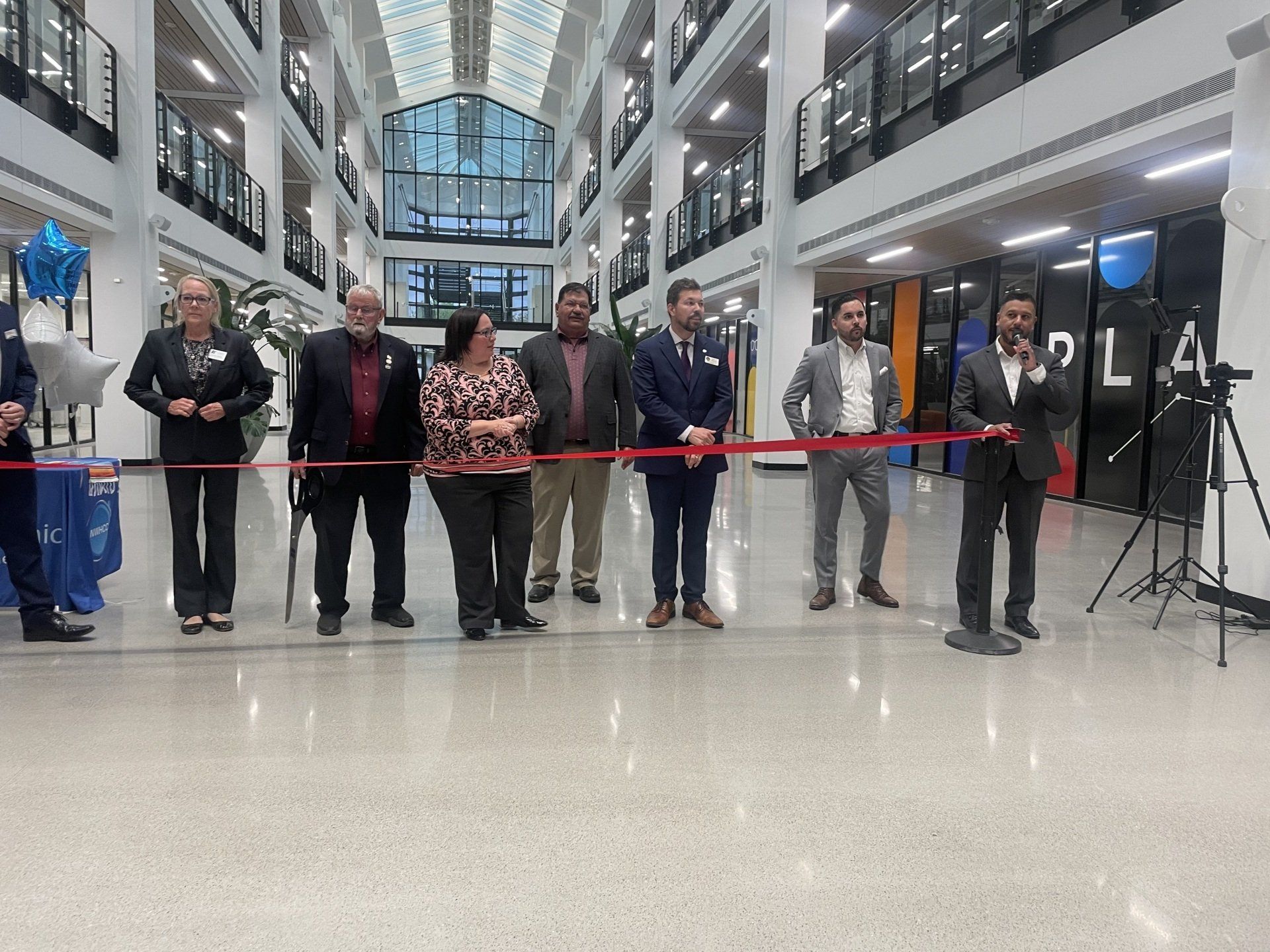 People standing in a modern atrium hold a red ribbon during a ribbon-cutting ceremony.