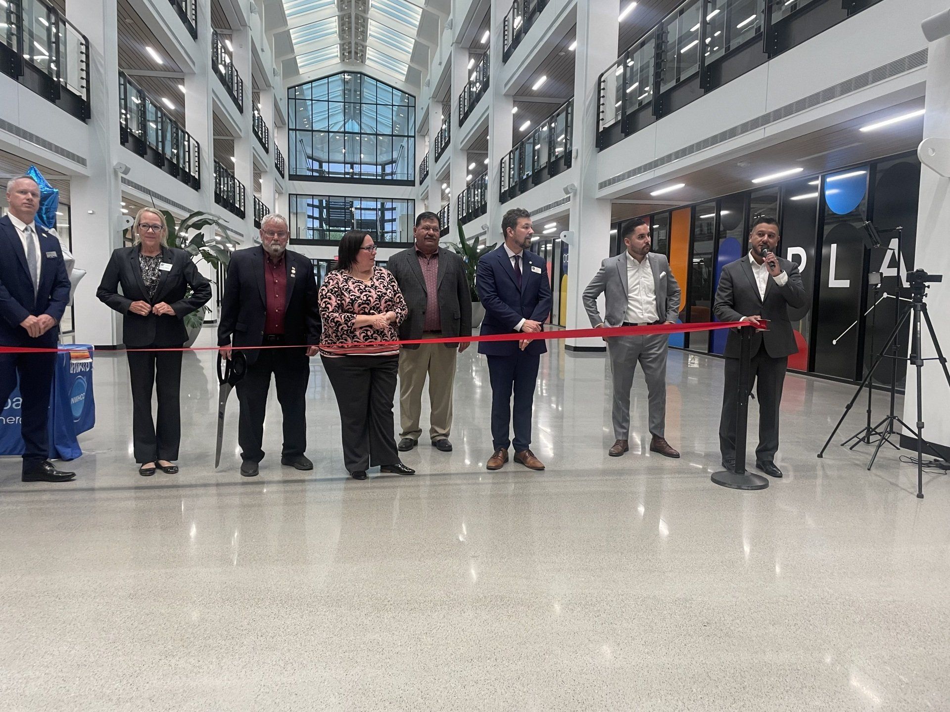 People lined up for a ribbon-cutting ceremony in a bright indoor atrium.