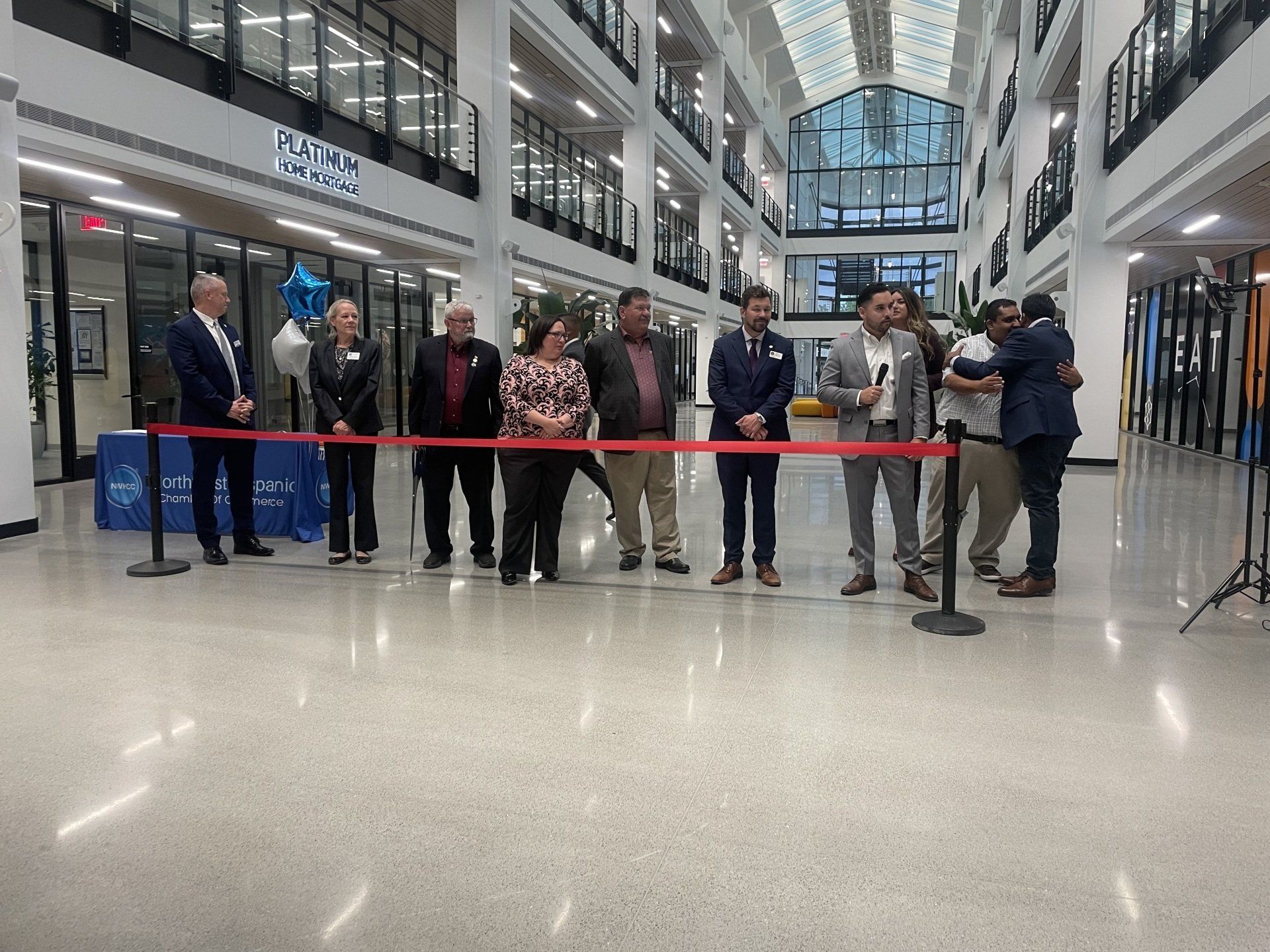 People standing behind a red ribbon in a bright indoor mall atrium, likely at a ribbon-cutting event.