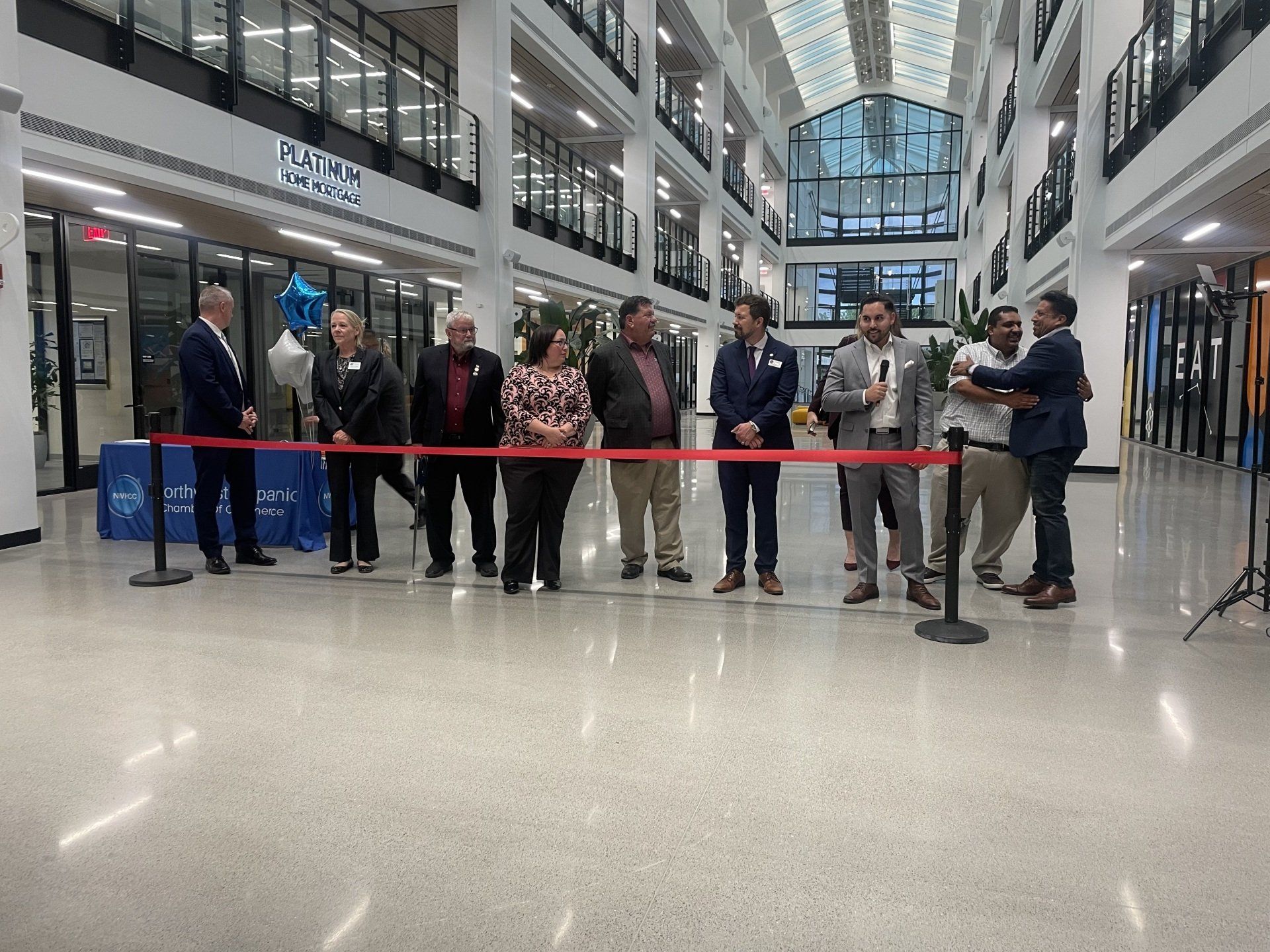 People gathered behind a red ribbon in a bright mall atrium during a ribbon-cutting ceremony