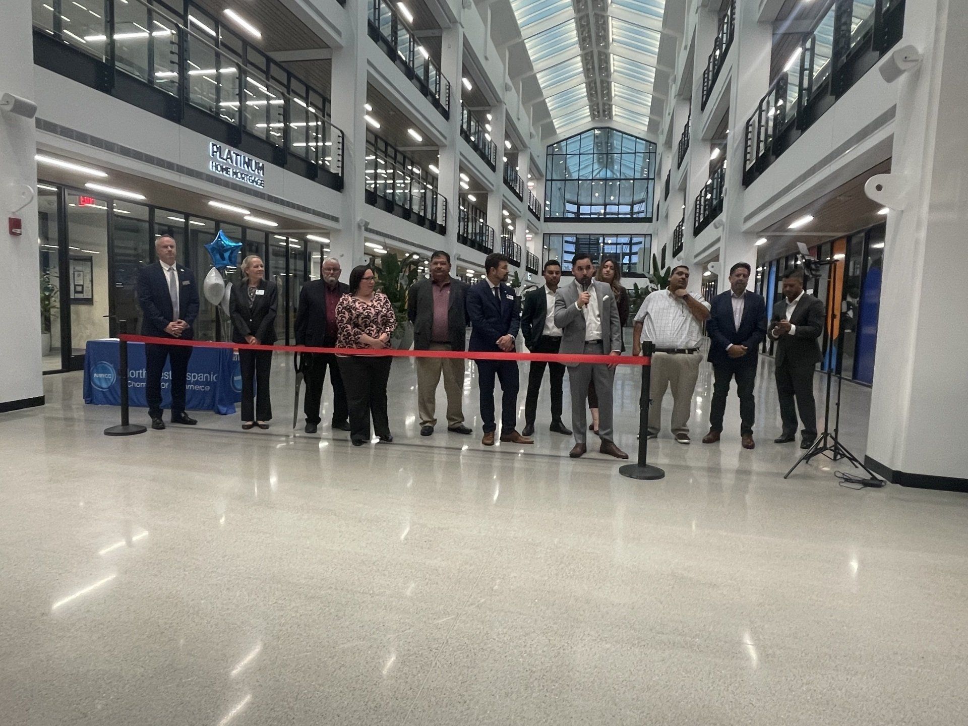 People gathered behind a red ribbon in a bright indoor atrium during a ceremony.