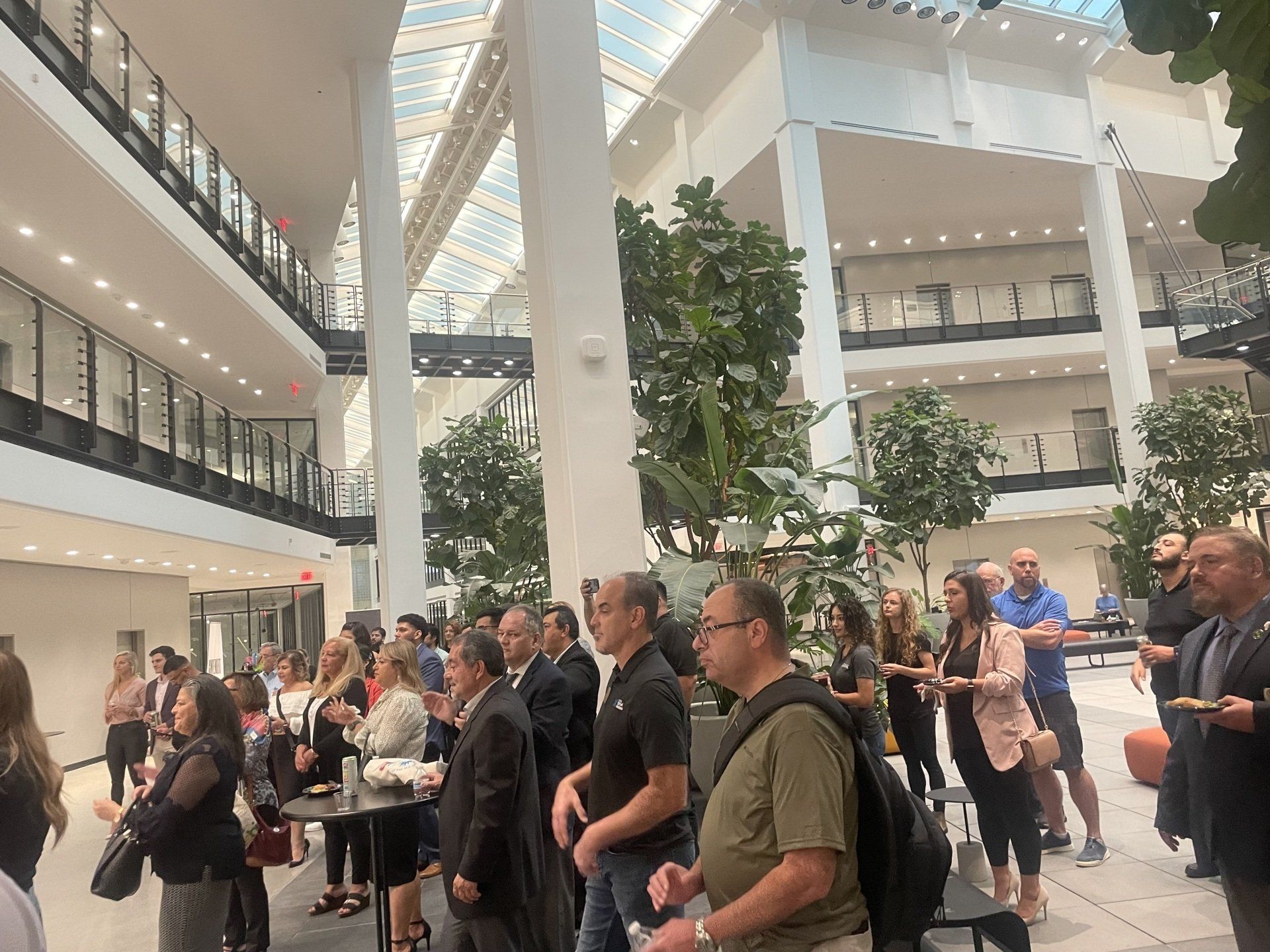 Crowded indoor atrium with people gathered near tall white columns and balconies under bright skylights