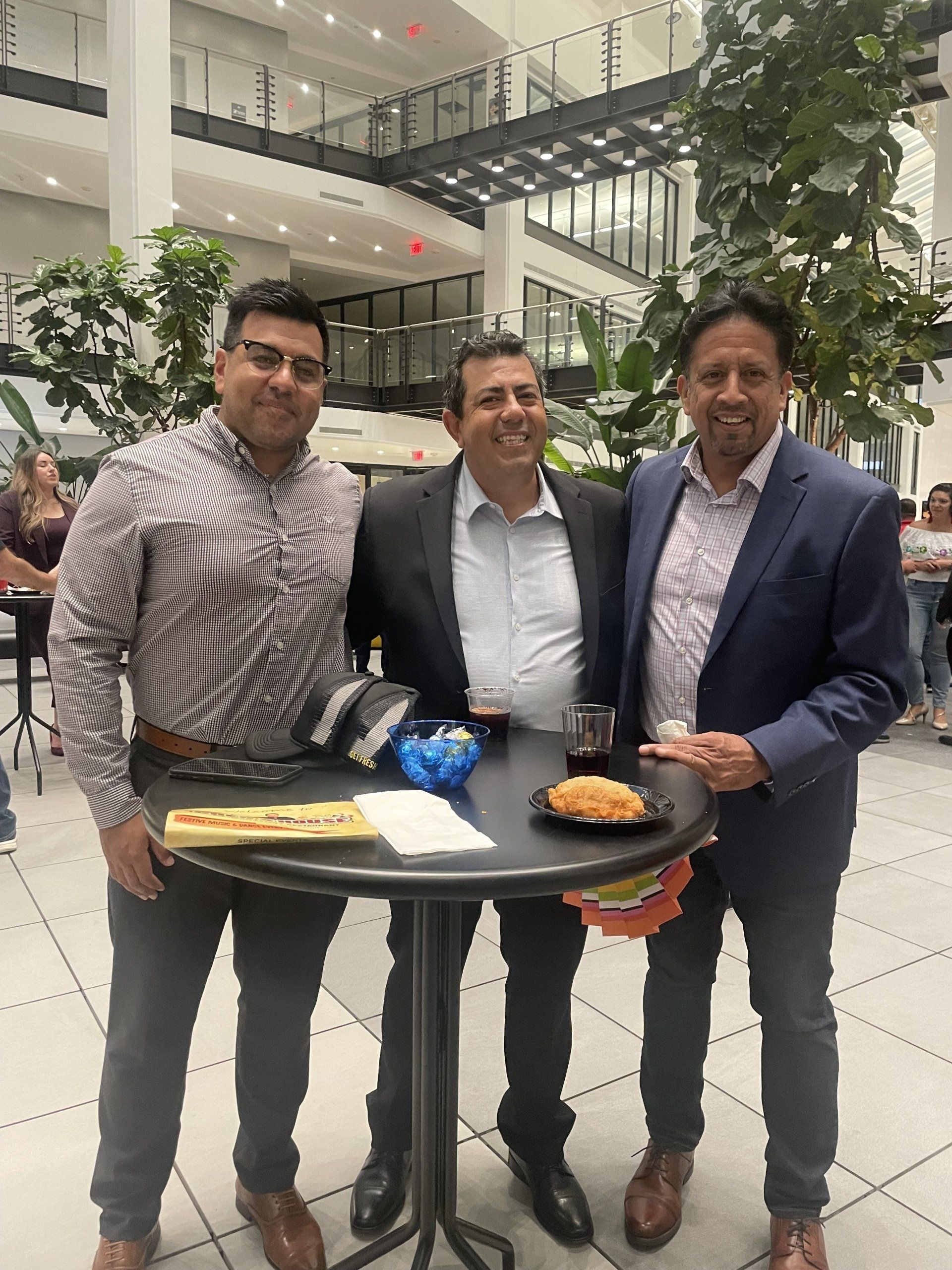 Three men posing with a tray of food in a bright indoor atrium