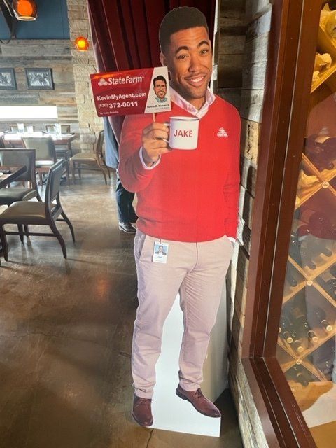 Life-size restaurant cutout of a smiling man in a red sweater holding a menu card by the entrance