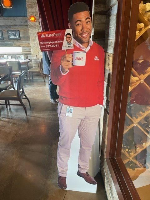 Cardboard cutout of a smiling man in a red top holding a sign inside a restaurant.