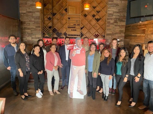Group of people posing indoors in front of a brick and wood wall, smiling for a group photo.