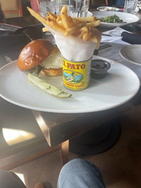 Burger and fries in a yellow cup on a white plate at a restaurant table.