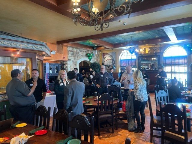 People mingling in a warmly lit restaurant dining room with wooden tables and chairs
