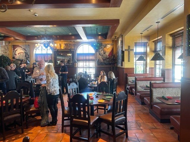 Dimly lit restaurant with people dining, dark wooden chairs, terracotta tile floor, and warm yellow walls