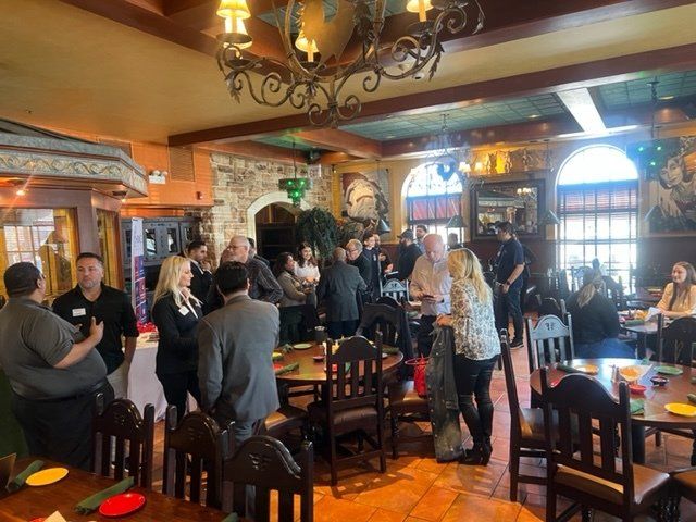 Crowded restaurant with people gathered around tables under warm chandeliers and stained-glass windows