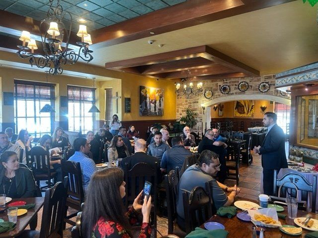 Busy restaurant dining room with seated patrons, warm lighting, and a server near the front.
