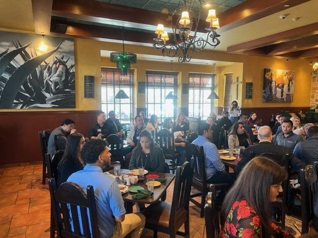 Crowded restaurant dining room with people seated at tables under warm chandelier lighting