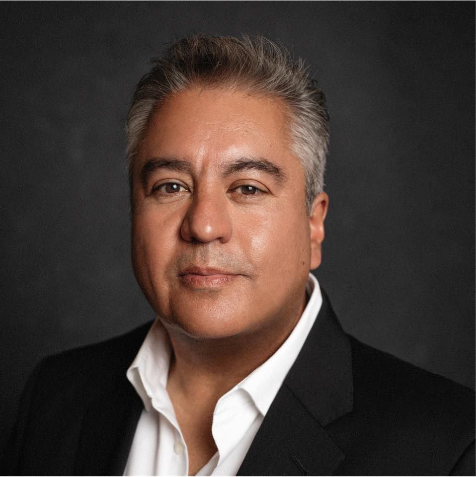 Studio headshot of a man in a black blazer and white shirt against a dark background