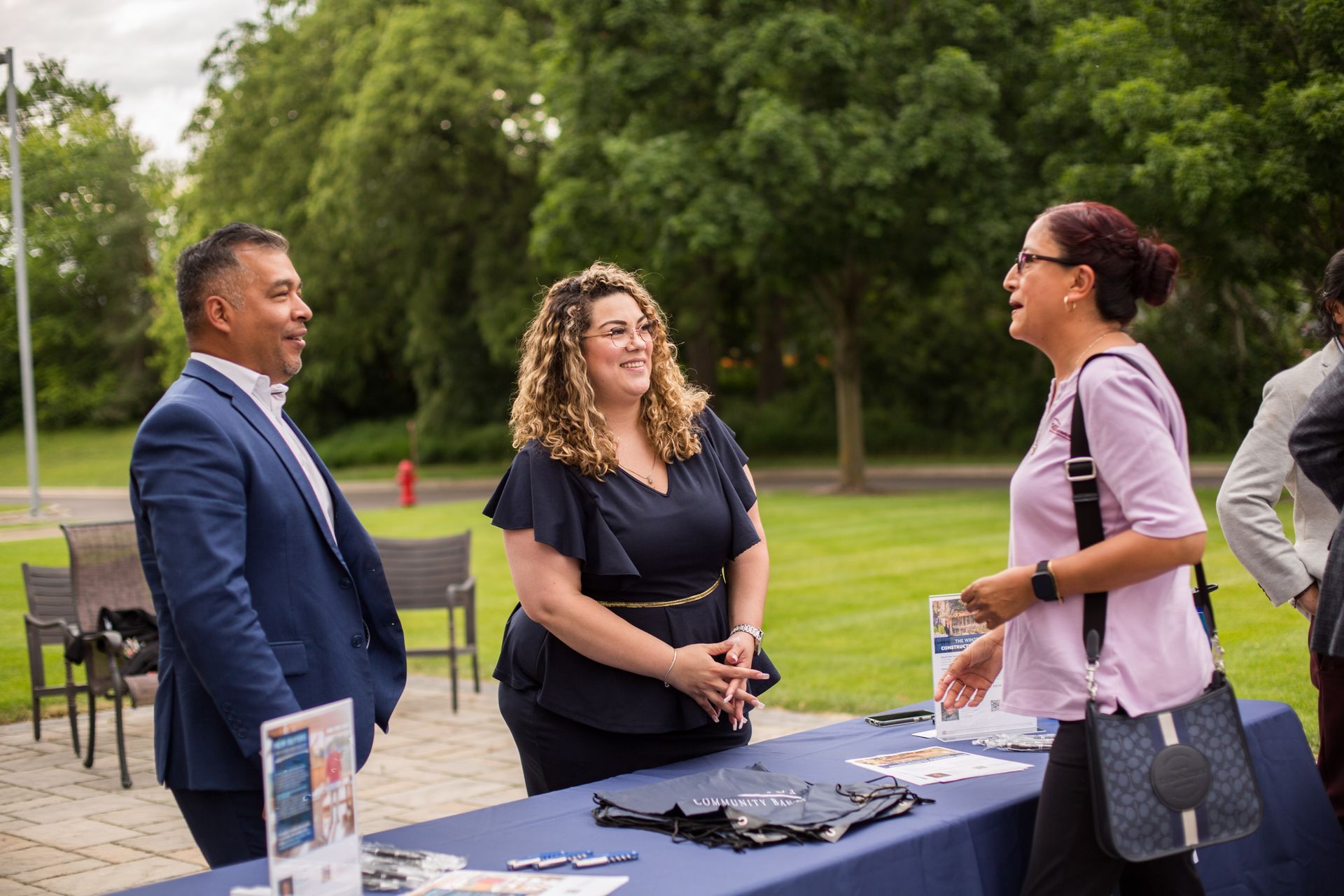 Three people talking at an outdoor event table in a park