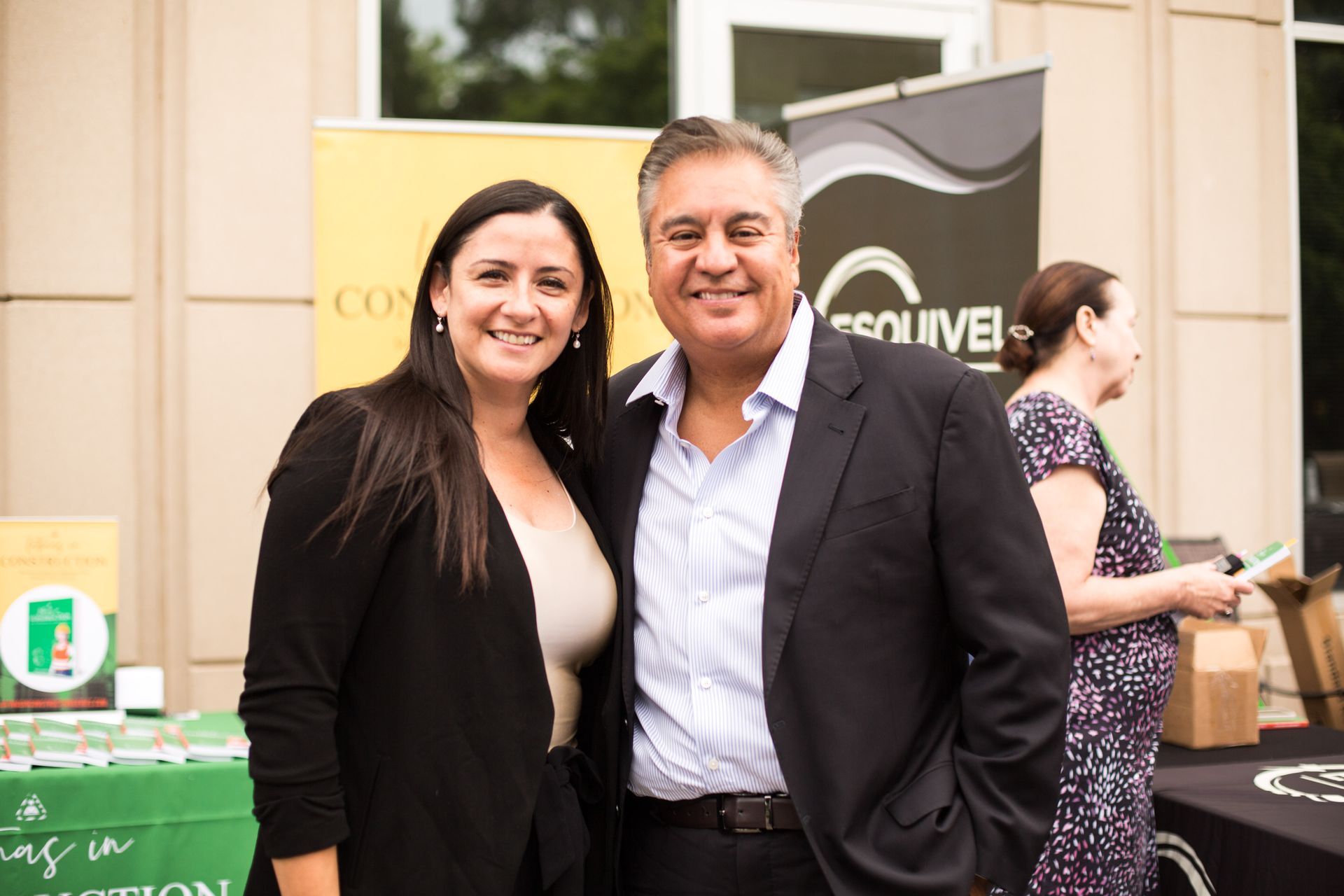 Two people smiling at an outdoor event booth with banners and promotional displays