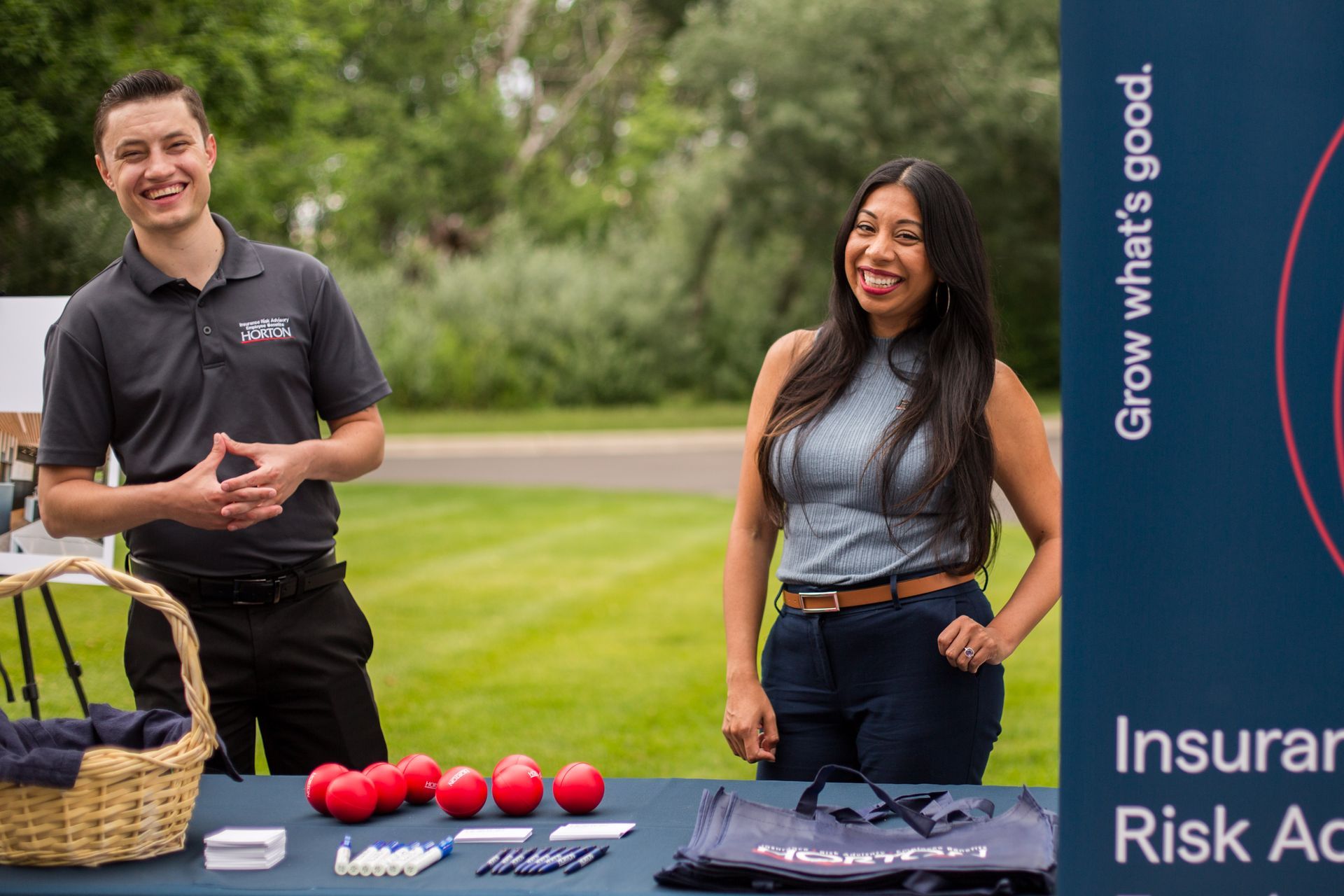 Two people stand behind a table with red balls at an outdoor event booth.