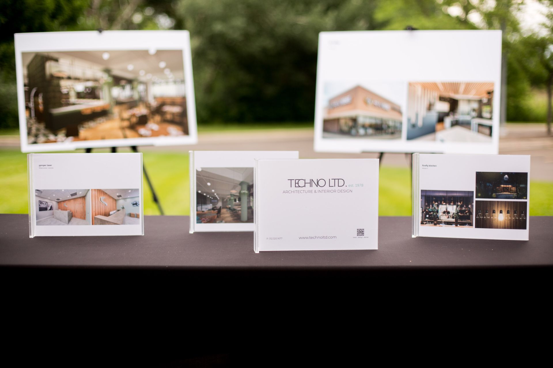 Design mockups for a building project displayed on a white table with architectural photos and brochures