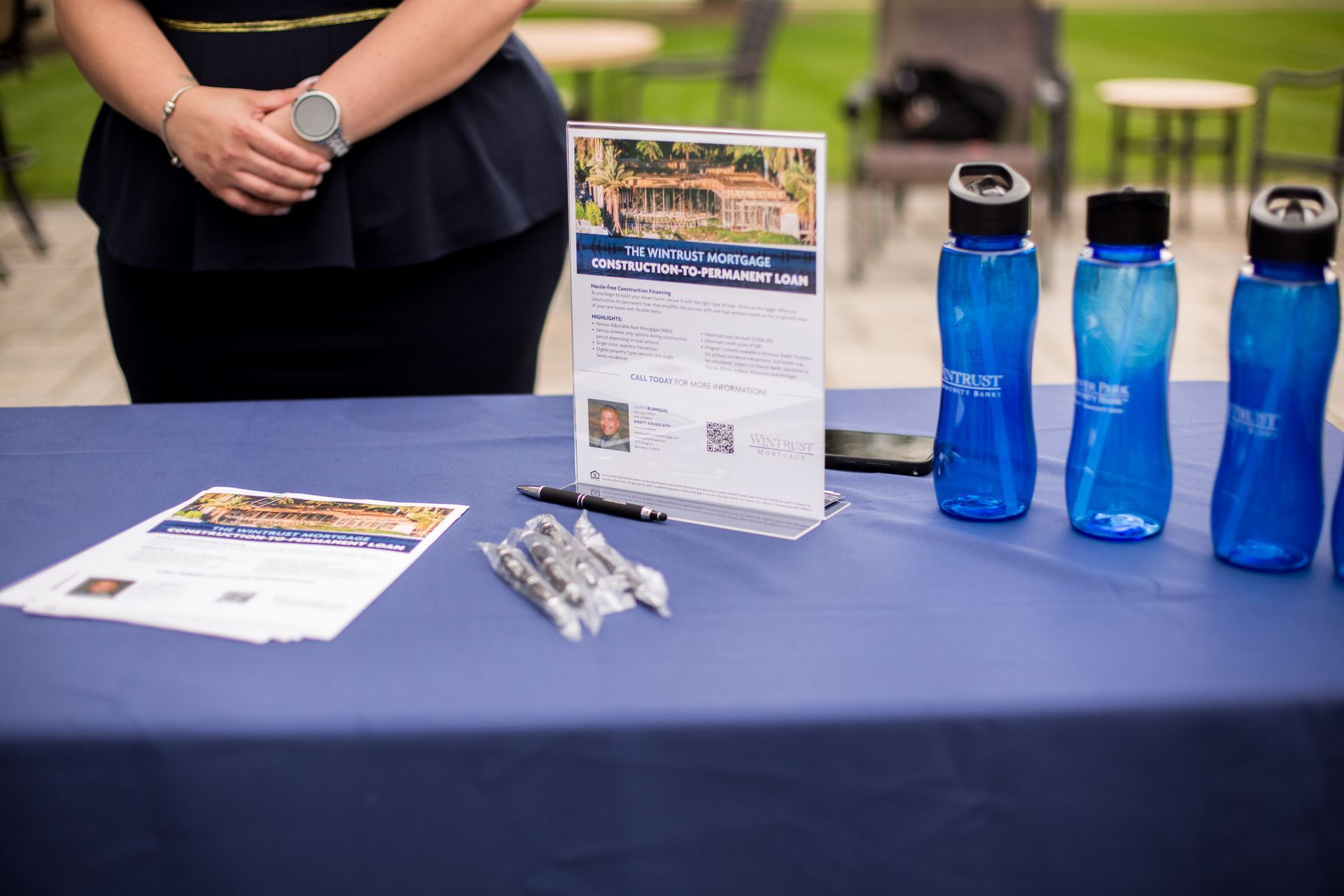 Table display with blue water bottles, pamphlet, and packets beside a person at an event booth