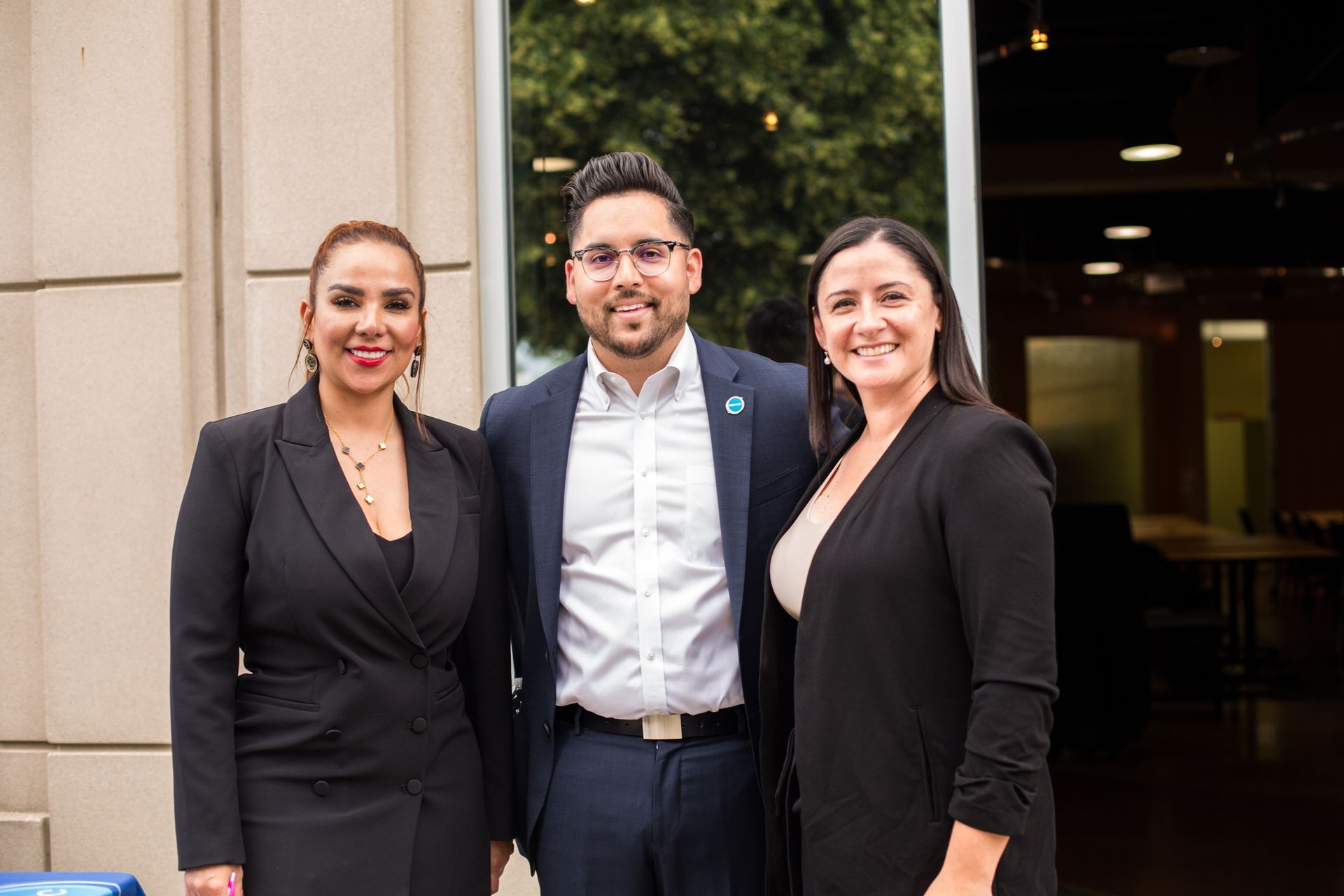 Three people standing together outside a building, smiling at the camera.
