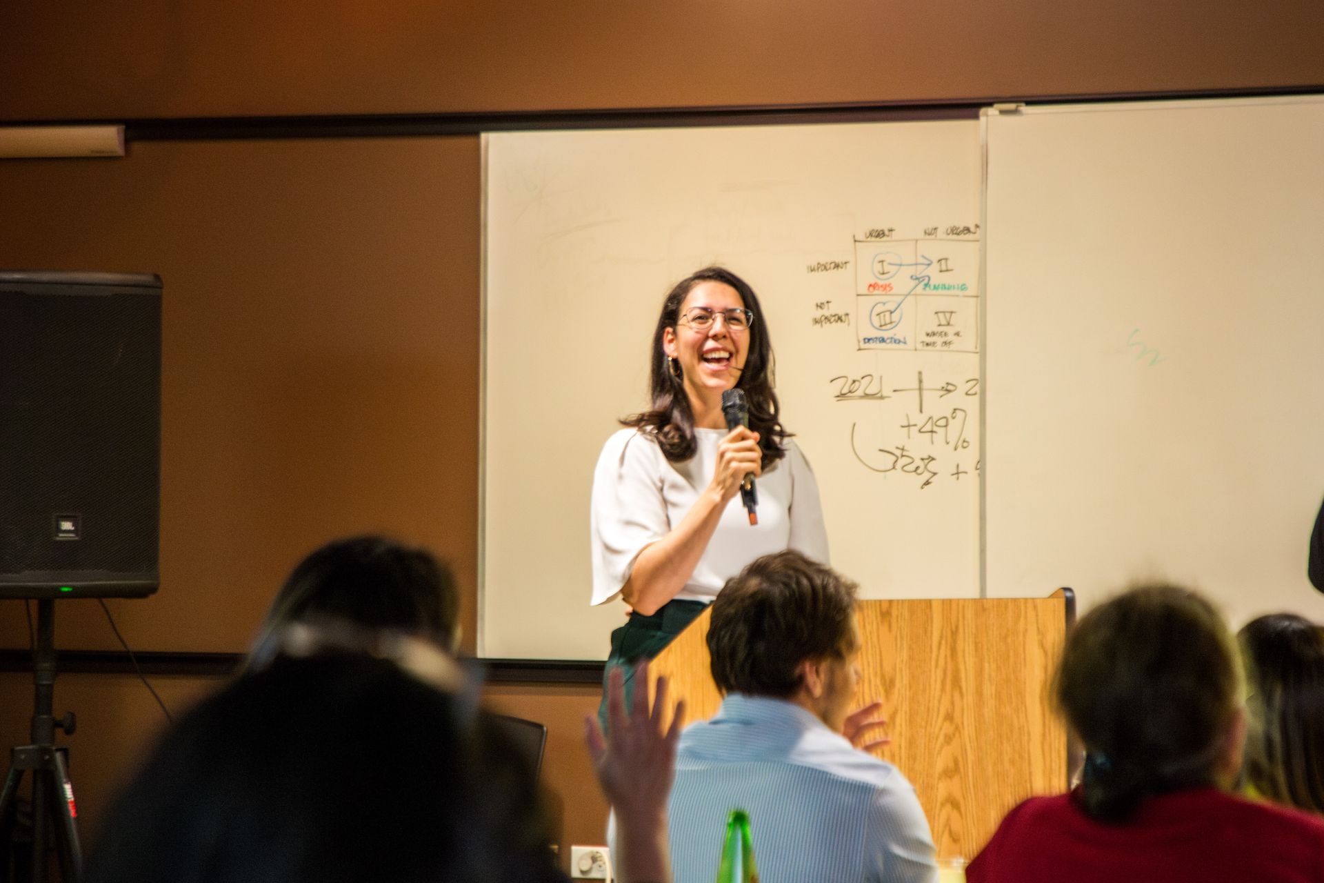 Speaker presenting at a podium in a conference room, with audience seated in the foreground.