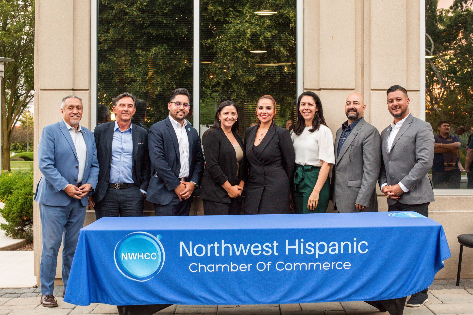 Group of people standing behind a blue “Northwest Hispanic Chamber of Commerce” banner outdoors