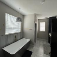 A modern bathroom featuring a white soaking tub, light gray walls, a hanging light fixture, and tile flooring.