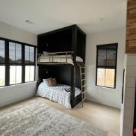 A modern bedroom featuring a black built-in bunk bed, a patterned rug, and large windows with black frames.