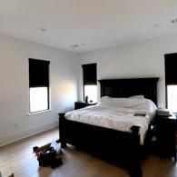 A bedroom with light walls and wood floors, featuring a dark wood bed frame and matching nightstands with black shades.