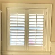 White plantation-style window shutters mounted inside a white wooden frame.